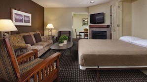 Ein Hotelzimmer mit einem Bett, einem Sofa, einem Sessel, einem kleinen Tisch mit Lampe, einem Fernseher und einem Kamin.