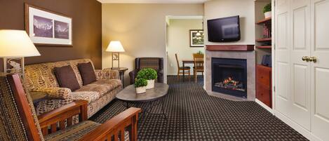 A living room with a sofa, armchair, coffee table, fireplace, television, and a dining area with chairs and a table.