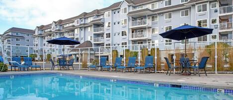 A swimming pool with lounge chairs and umbrellas, surrounded by multi-story residential buildings.