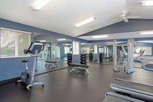 Un gimnasio con equipo de ejercicio, espejos y un ventilador de techo.