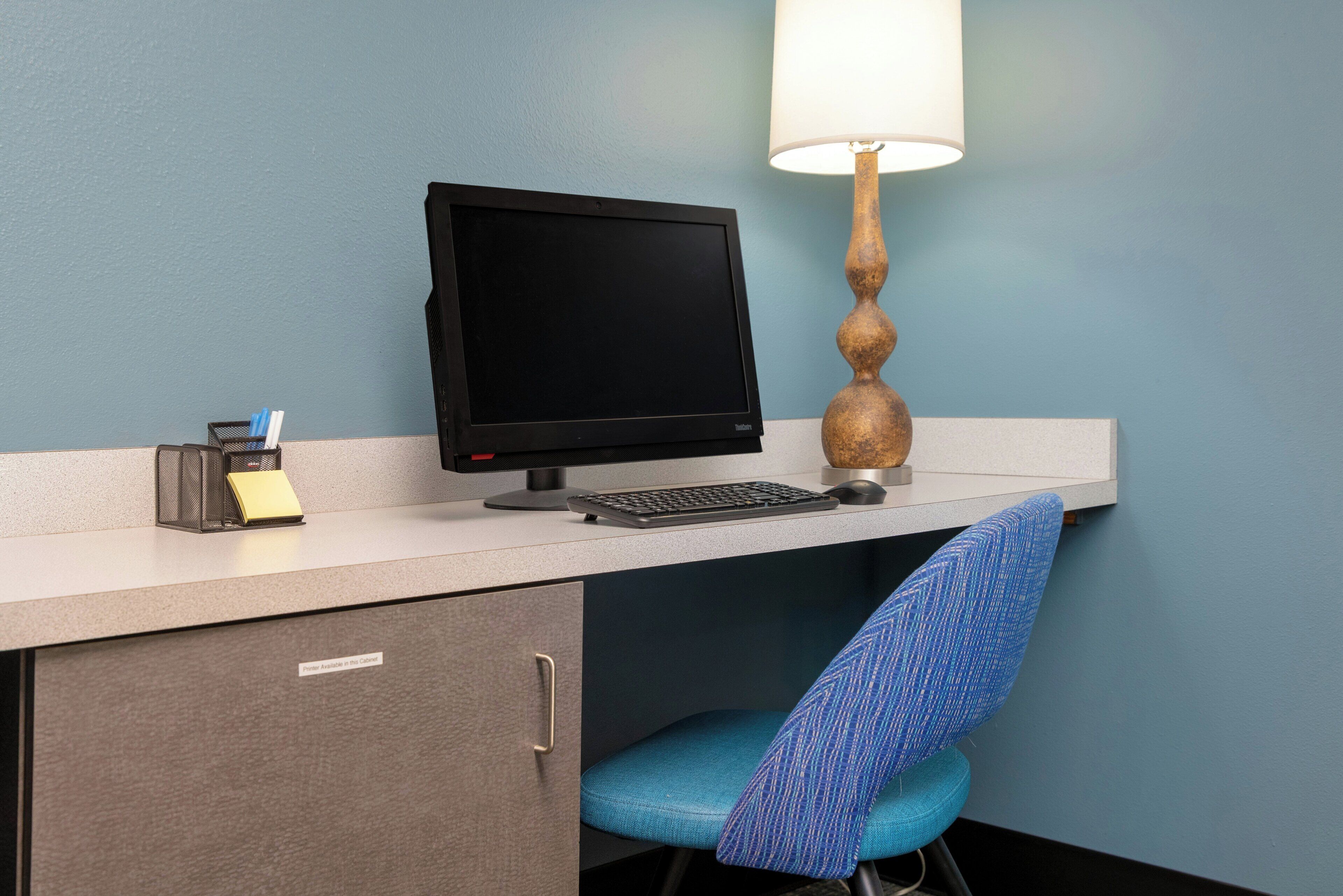 A desk with a computer, a lamp, a chair, and a small storage box.