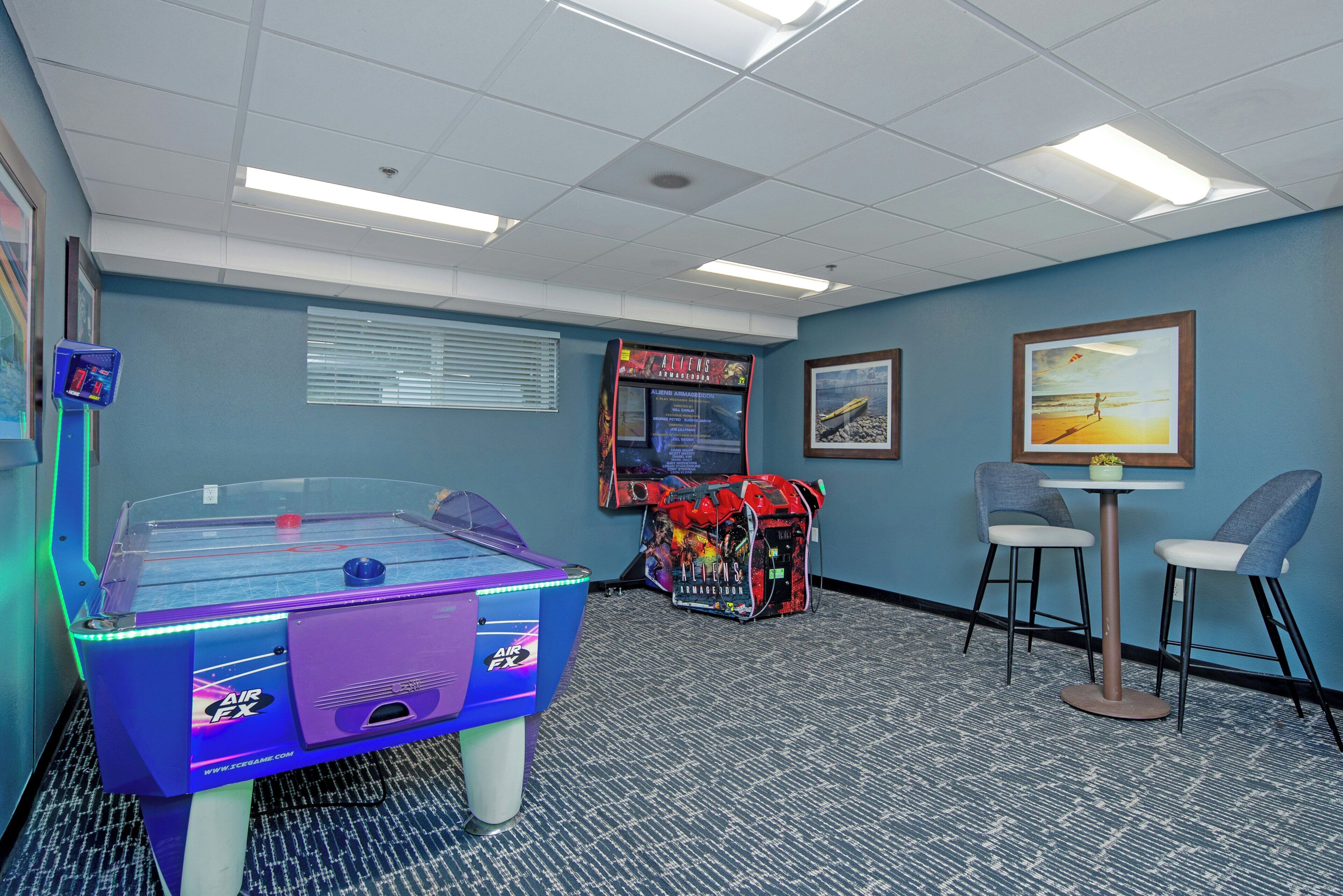 Une pièce avec un baby-foot, une console de jeux vidéo et une petite table avec des chaises.