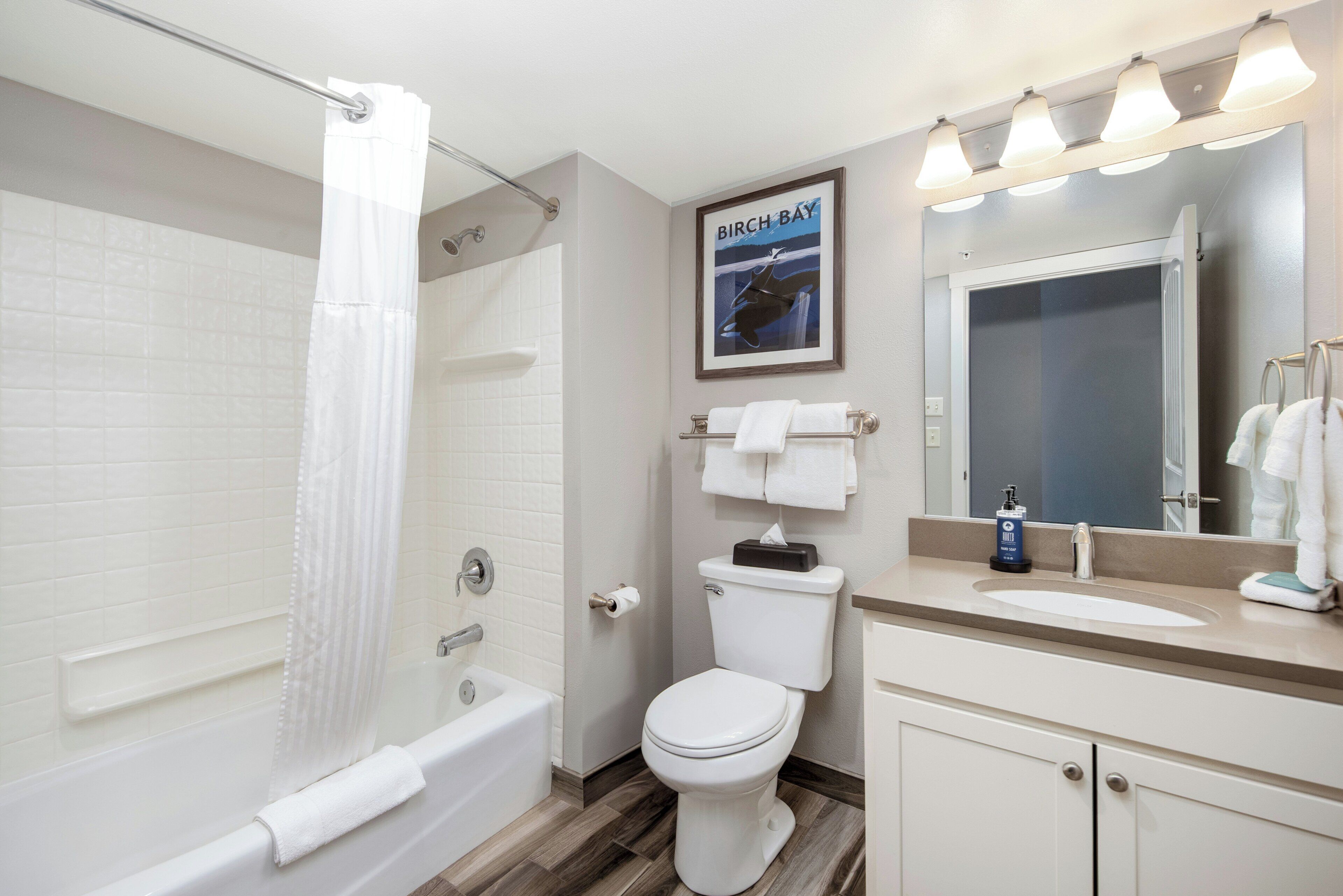 Een badkamer met bad, toilet, wastafel en een spiegel met verlichting.
