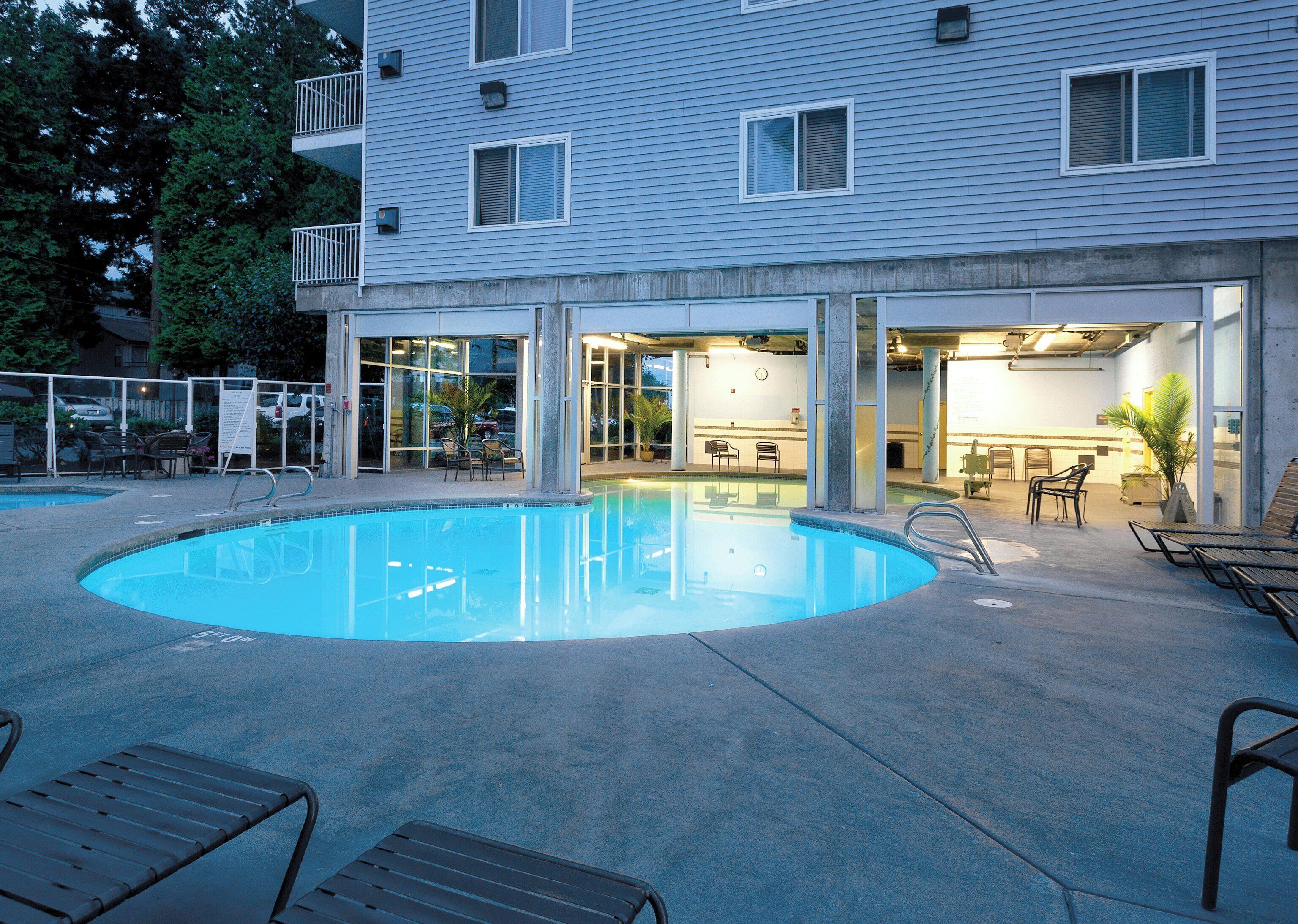 A swimming pool with lounge chairs, a bar area, and a building with multiple windows and balconies.