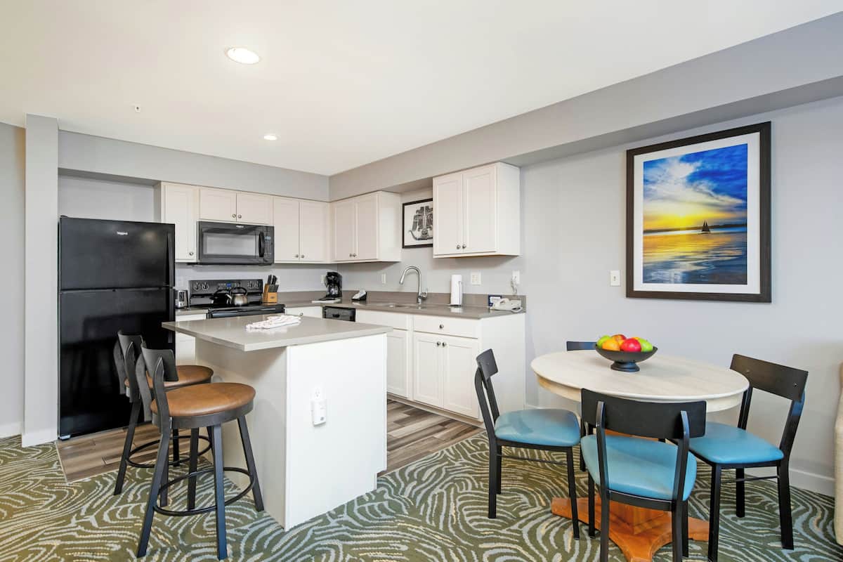 A modern kitchen with white cabinets, a black refrigerator, and a dining area with a round table and blue chairs.