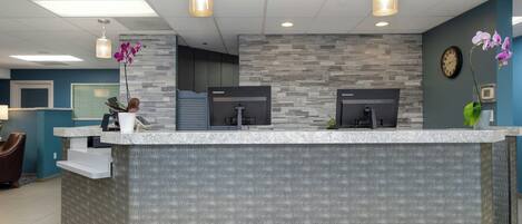 A reception desk with a stone wall backdrop, two monitors, and a clock on the wall.