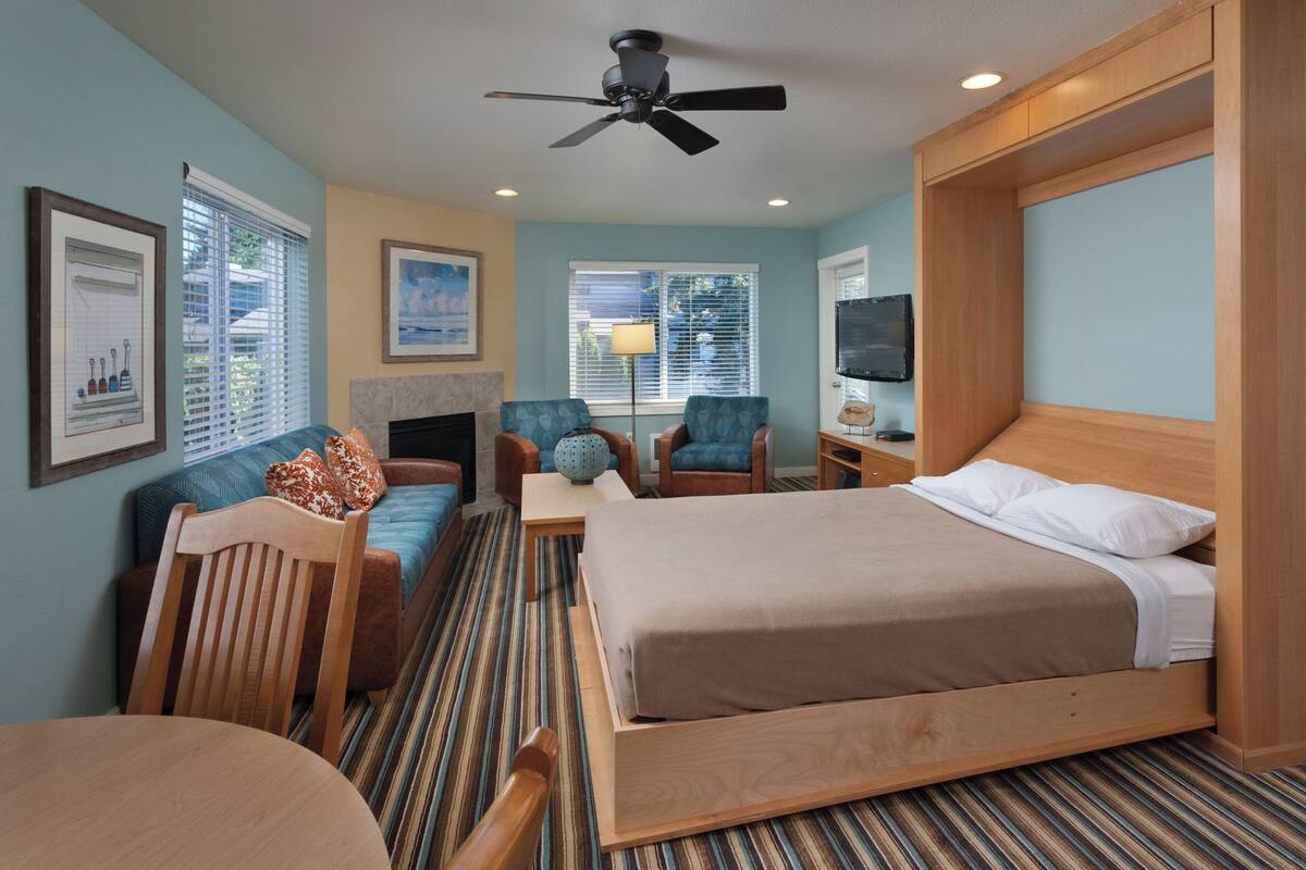 A hotel room with a bed, two armchairs, a table, and a ceiling fan.