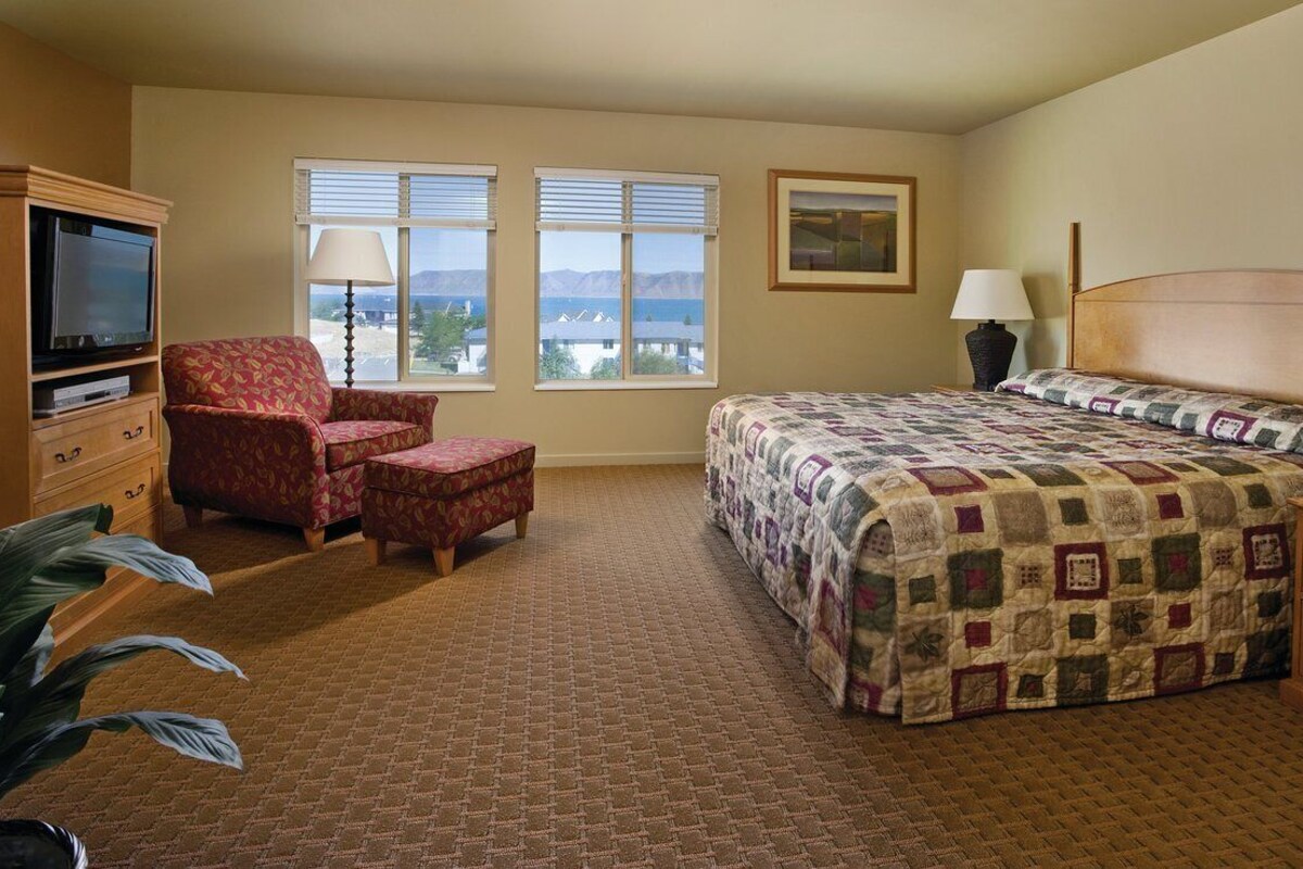 A hotel room with a large bed, a TV, a chair, and a view of the mountains.