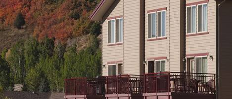 A two-story house with a balcony, a stone foundation, and a hillside in the background.