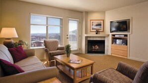 A living room with a sofa, armchair, coffee table, fireplace, TV, and a view of the city. - WorldMark Bear Lake (Garden City)