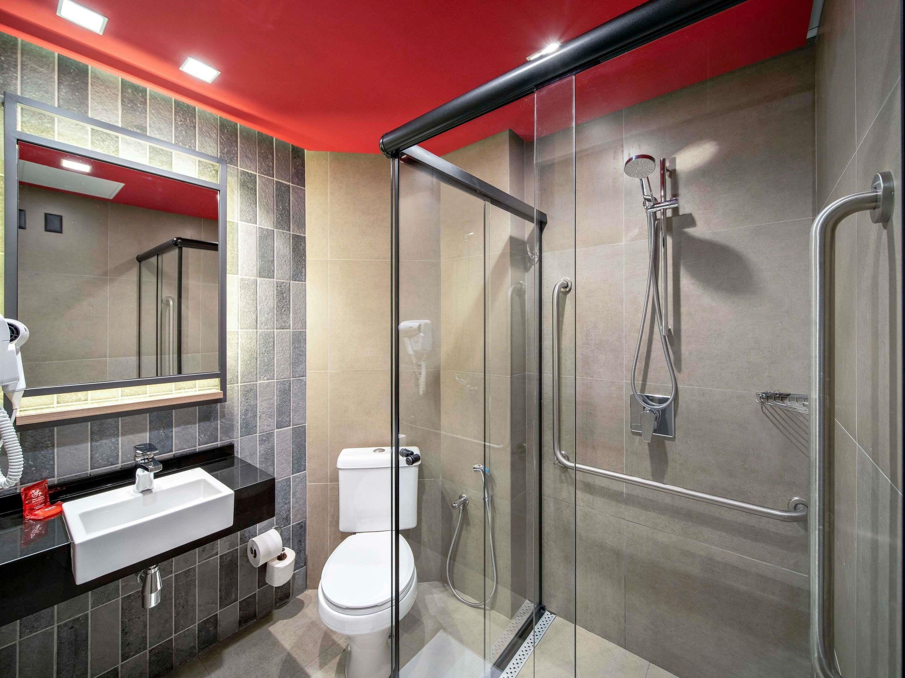 Un baño moderno con ducha de vidrio, inodoro blanco y lavamanos negro con espejo superior.