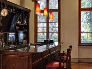 A bar area with a wooden counter, shelves with bottles, and hanging orange pendant lights. - ibis Curitiba Batel (Curitiba)