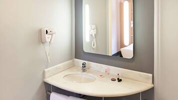 A bathroom with a sink, a mirror, a hairdryer, and a towel.