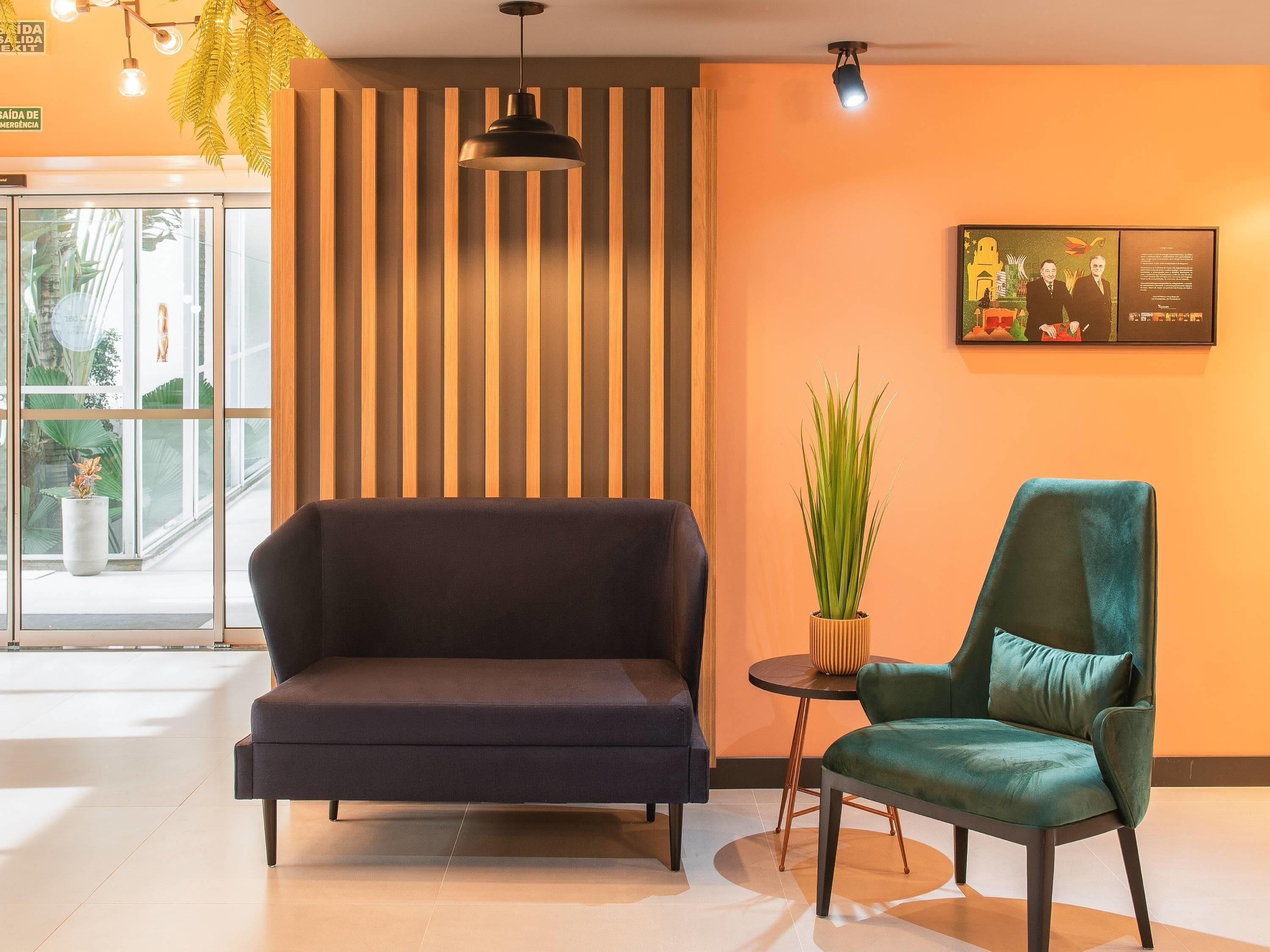 A lobby with a dark sofa, a green armchair, a potted plant, and a framed picture on the wall.