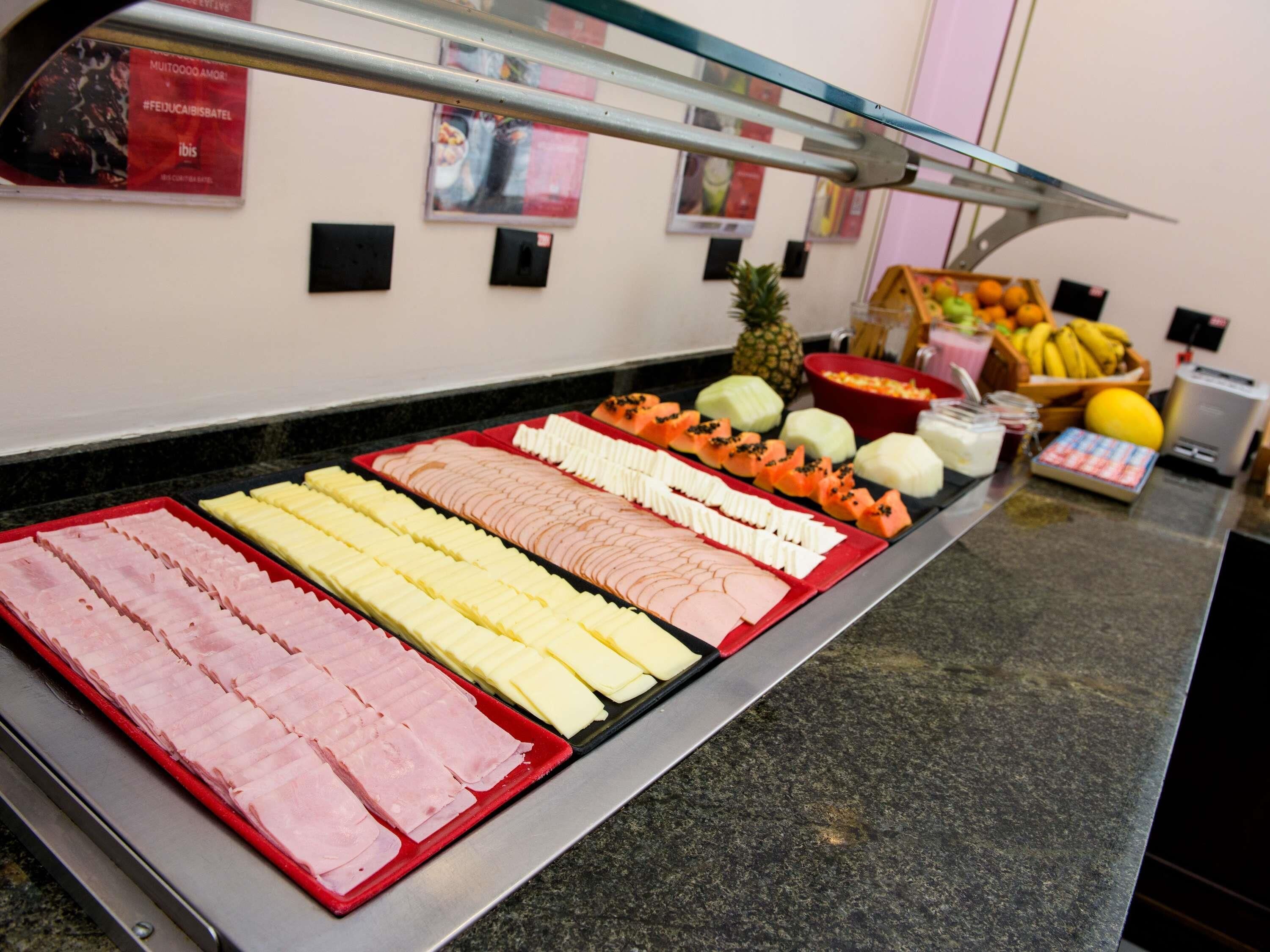 A buffet with various meats and cheeses, a fruit display, and a weighing scale.