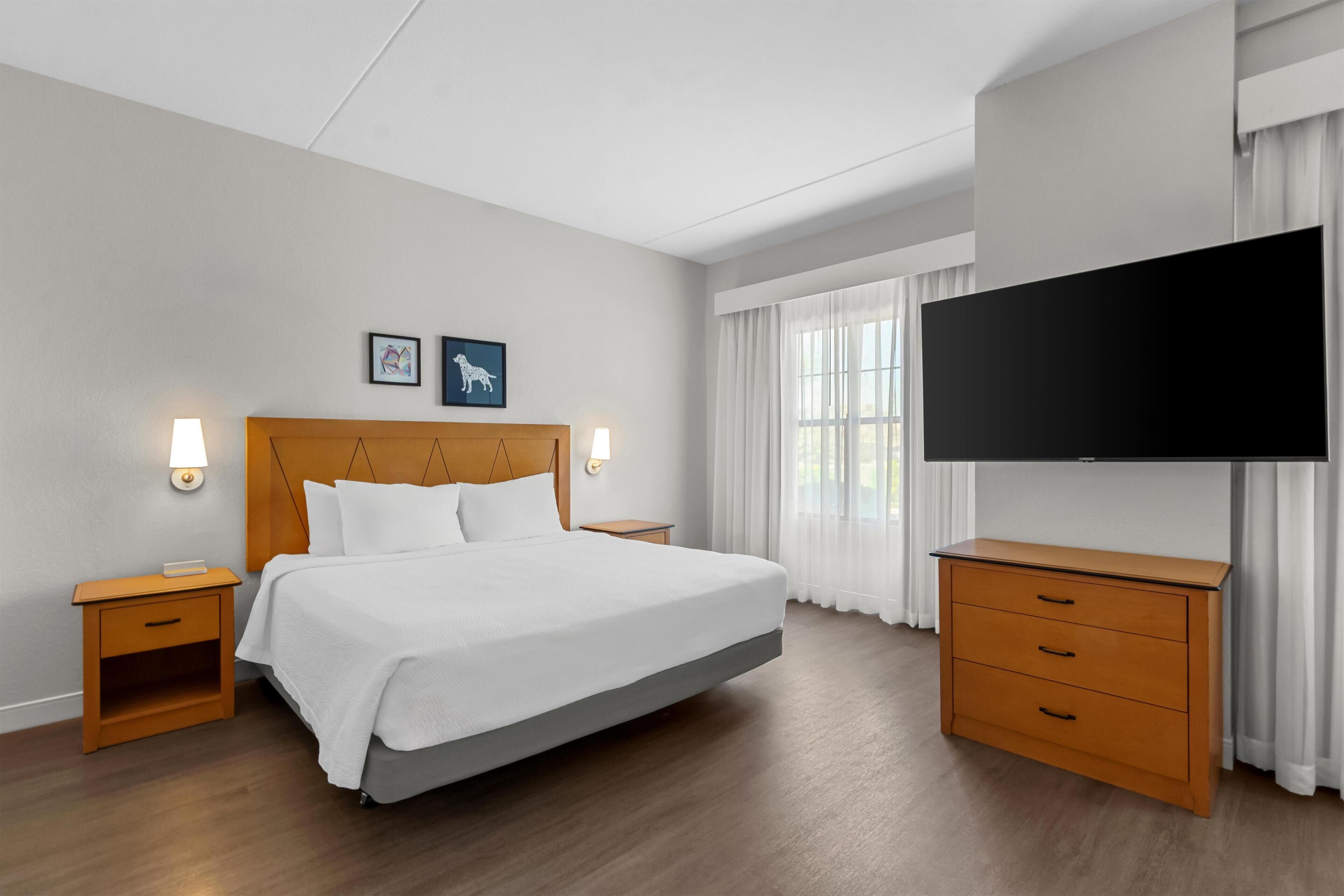 Hotelkamer met een groot bed, houten hoofdeinde, twee nachtkastjes, een flatscreen televisie en een houten dressoir.