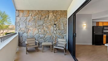 Un balcon avec un mur en pierre, une porte coulissante noire donnant sur une cuisine et deux chaises en bois.