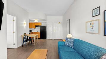 Un salon avec un canapé bleu, une table basse en bois et une cuisine en arrière-plan.