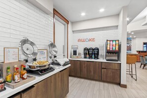 A kitchen area with a coffee station, a sign reading 'AWOKE,' and a 'FARM TO TABLE Classics' sign.