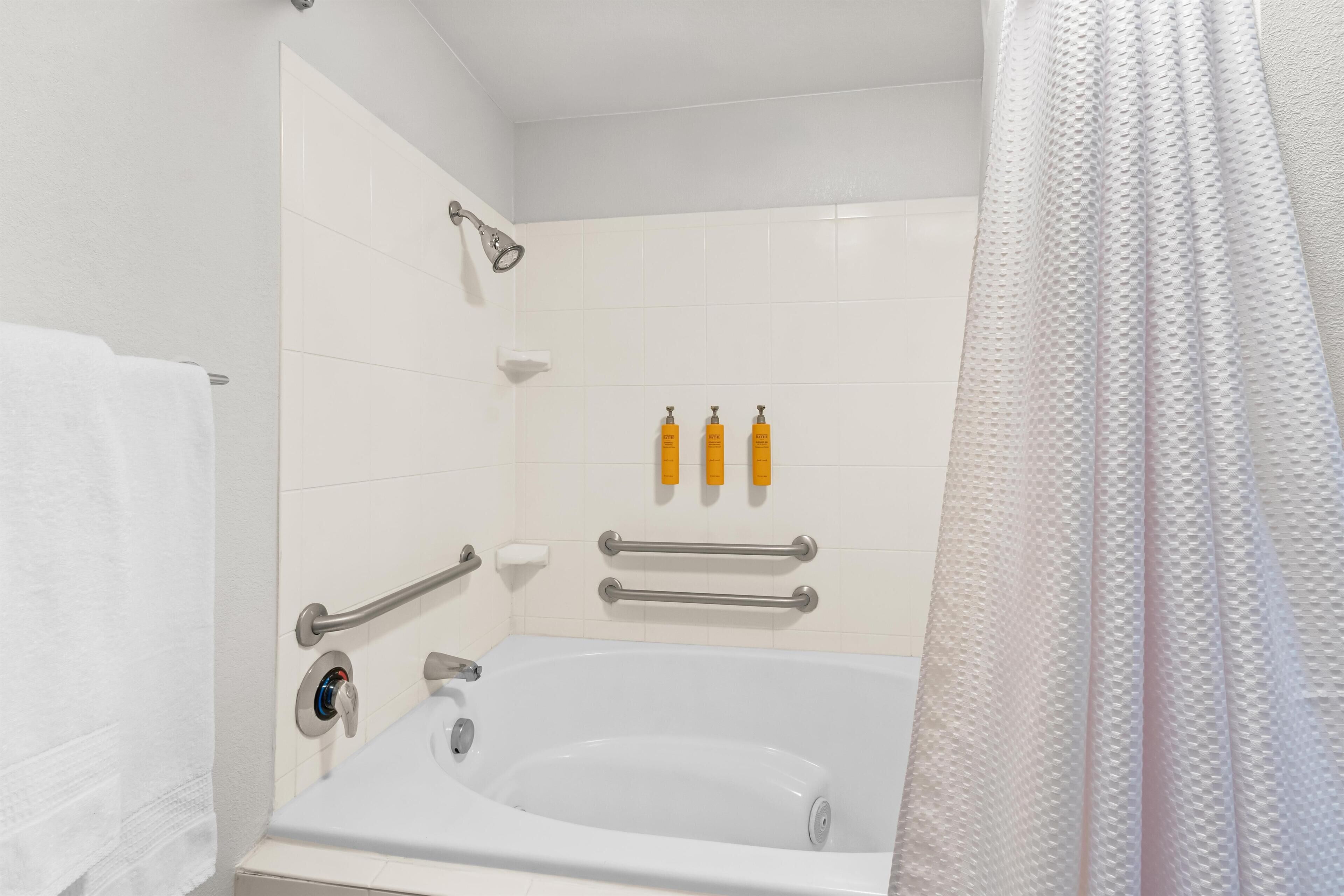 A white bathroom with a bathtub, grab bars, and a shower curtain.