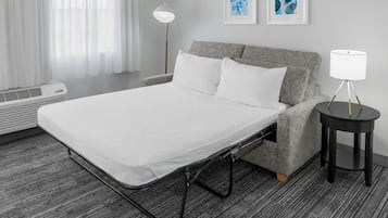 A hotel room with a bed, a bedside table with a lamp, a wall-mounted air conditioner, and two framed artworks.