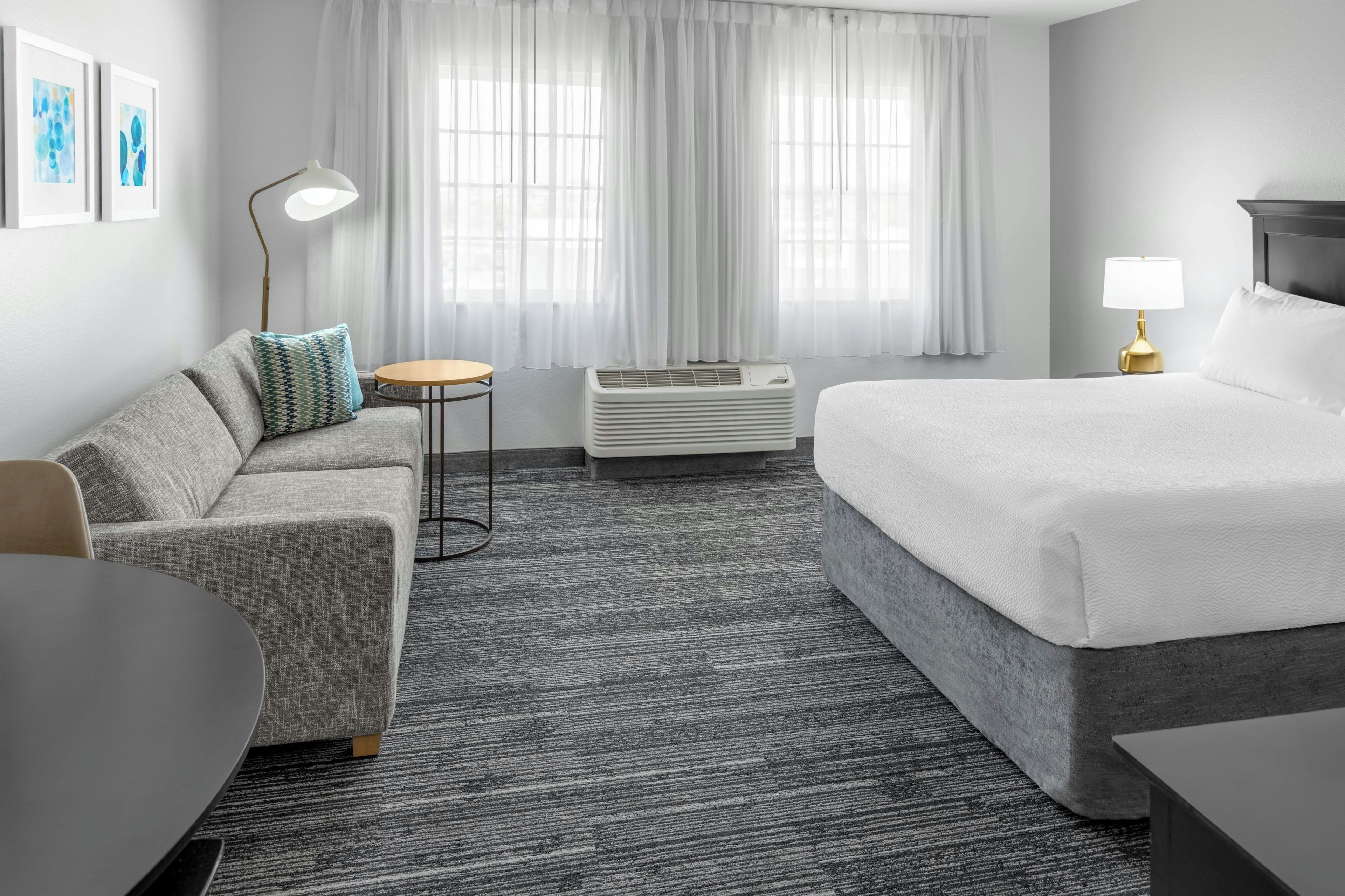 Habitación de hotel con cama, sofá, una mesita, lámpara y aire acondicionado.
