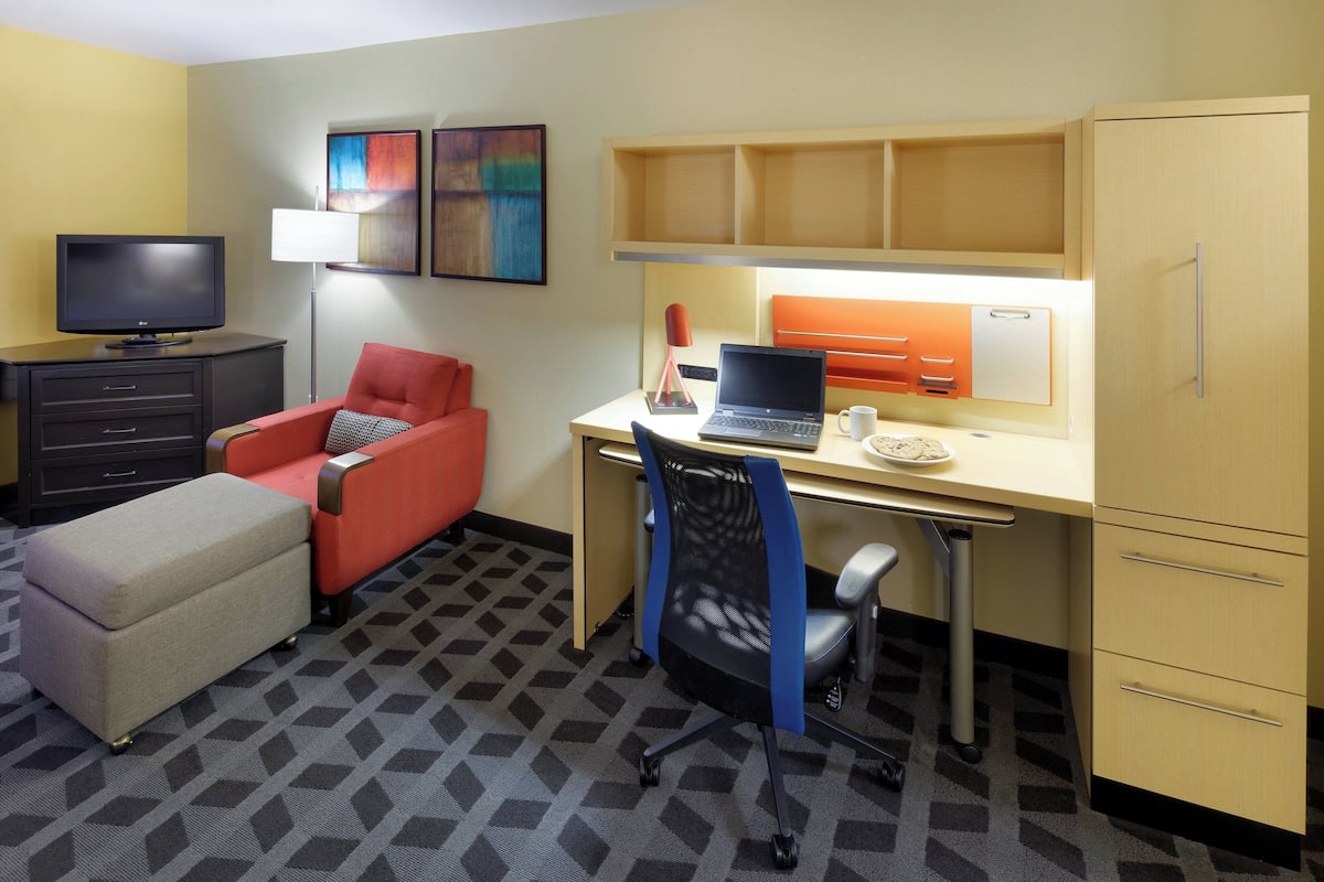 A hotel room with a desk, a chair, a television, a sofa, and a bed.