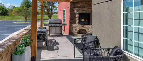 An outdoor patio with a grill, seating, and a stone fireplace.
