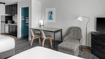 A hotel room with a bed, a desk, two chairs, a television, a desk lamp, and a microwave.