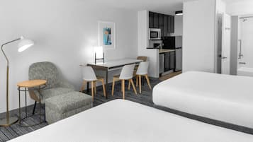 A hotel room with a bed, a desk with chairs, a kitchenette, and a bathroom.