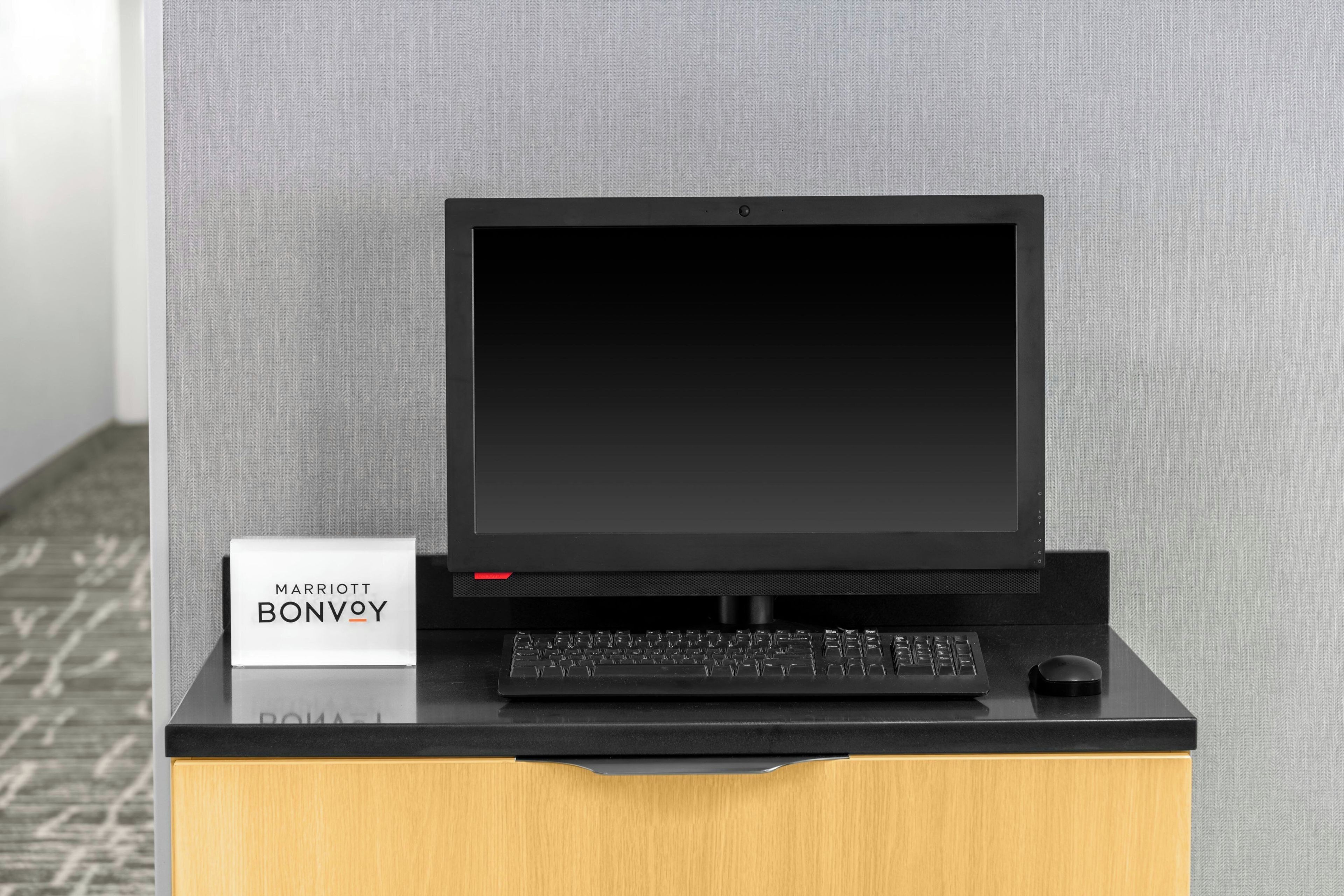 A black laptop on a wooden stand with a keyboard, a sign reading 'MARRIOTT BONVOY', and a grey textured wall in the background.