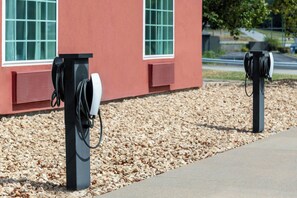 Twee laadpunten voor elektrische voertuigen met kabels en een rood gebouw op de achtergrond.