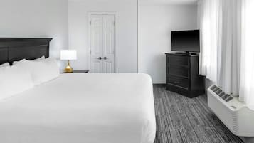Quarto de hotel com uma cama grande, mesa de cabeceira com abajur, cômoda, televisão e janela com cortinas.