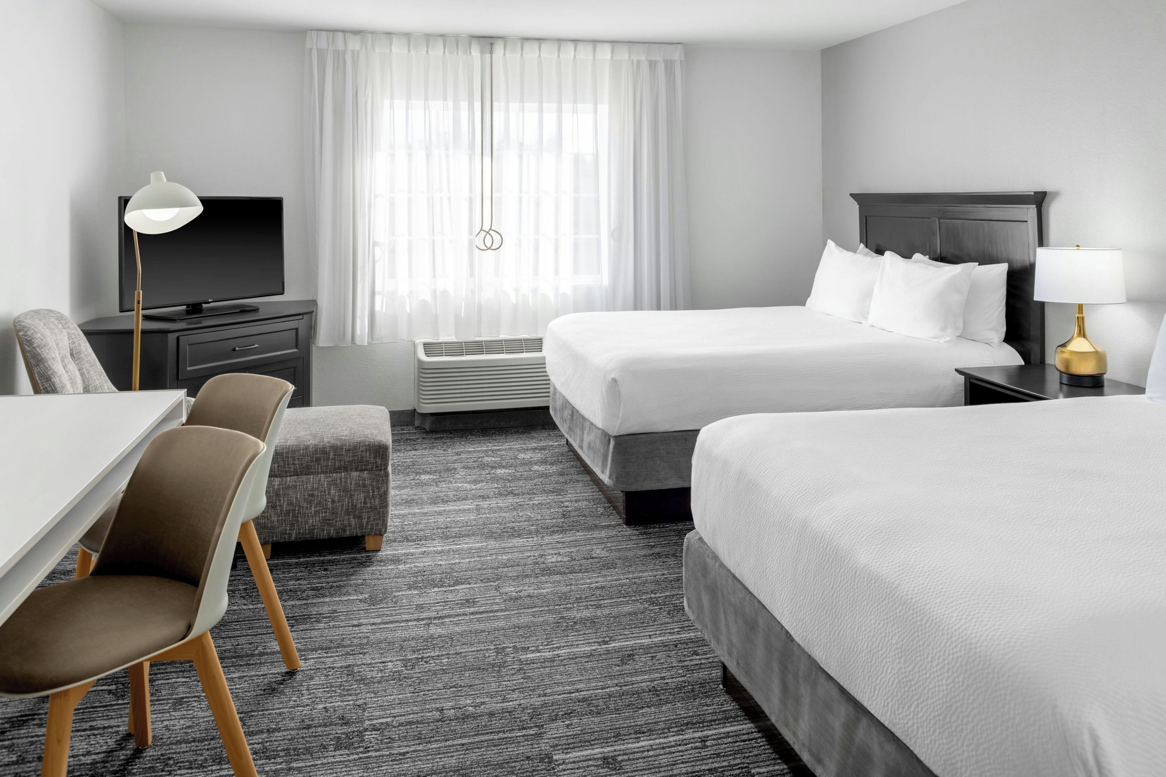 A hotel room with a bed, a desk, a chair, a TV, and a lamp.