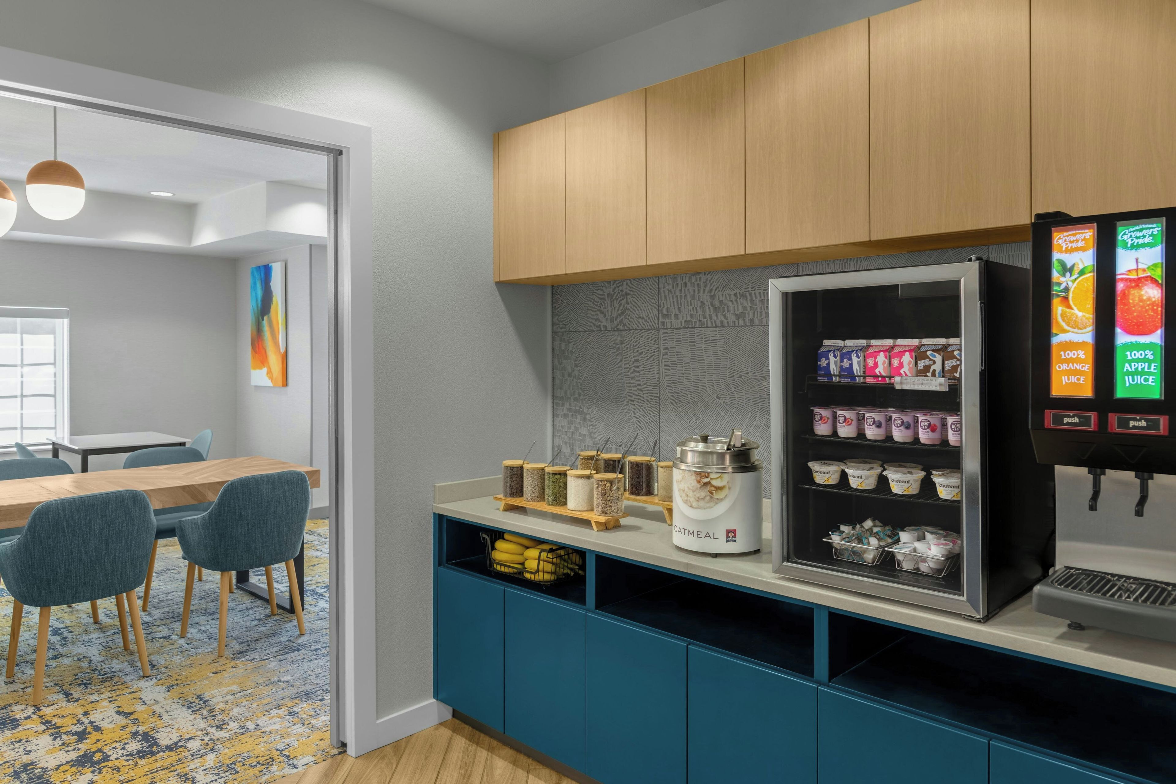 A kitchenette with a refrigerator stocked with beverages and food items, a coffee machine, and a small dining area with chairs and a table.