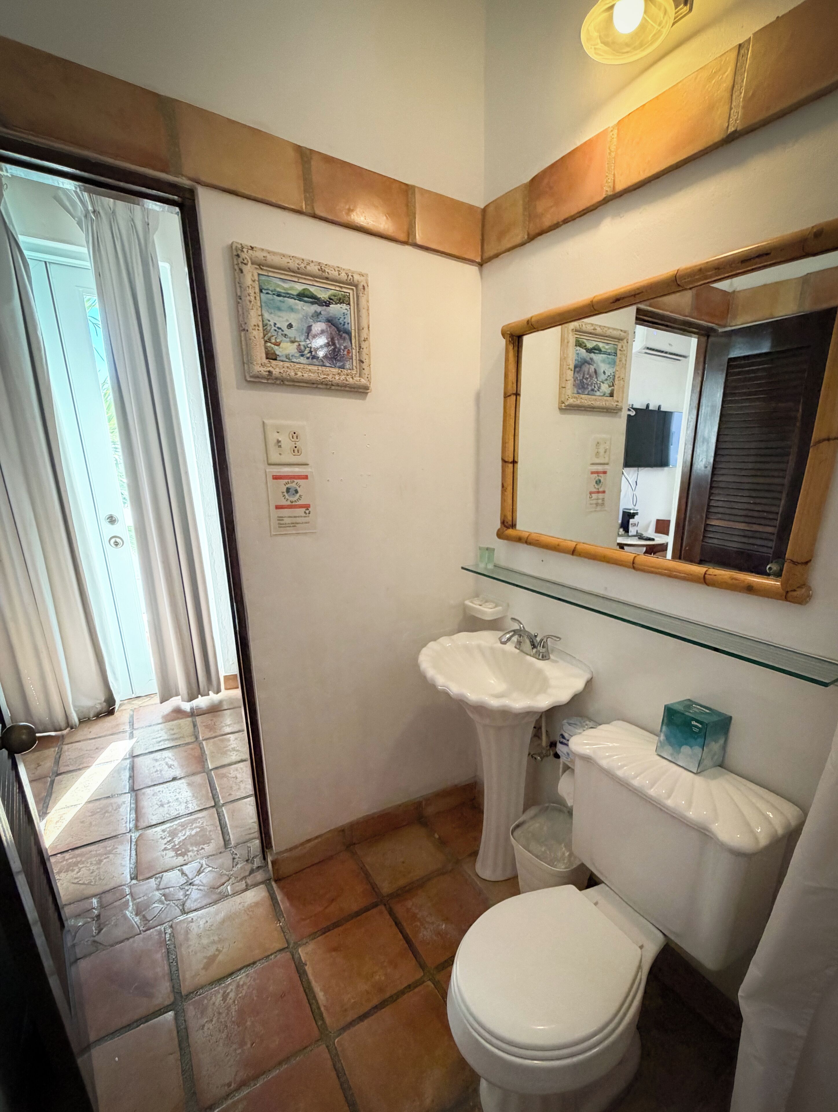 A bathroom with a white sink, toilet, and a mirror above the sink. There are two framed pictures on the wall and a glass shelf above the sink.