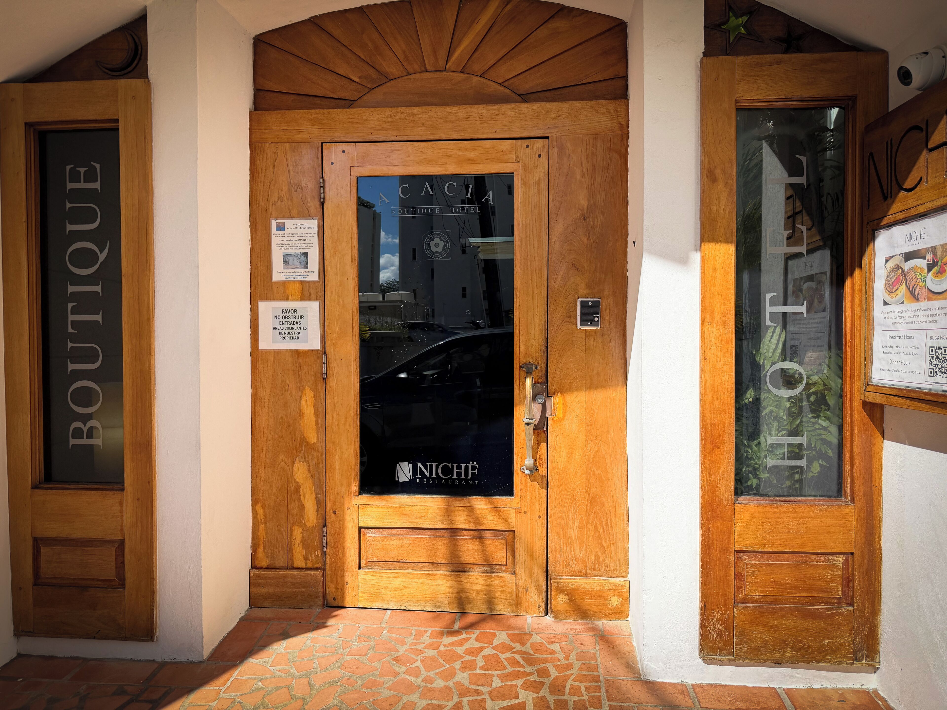 A wooden hotel entrance with a sign reading "NICHÉ RESTAURANT" and a sign above the door stating "FAVOR NO OBSTACLES ENTRADAS AREAS CONDICIONADAS PROPIEDAD".