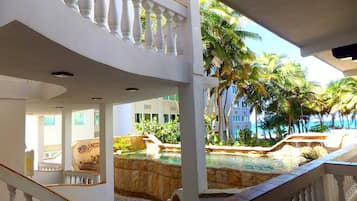 L’intérieur d’un hôtel avec un espace piscine, des balustrades blanches et une vue sur des palmiers.