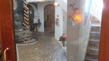 Pasillo con suelo de piedra que lleva a un restaurante, con una estatua de Buda, una escalera y una puerta de madera.