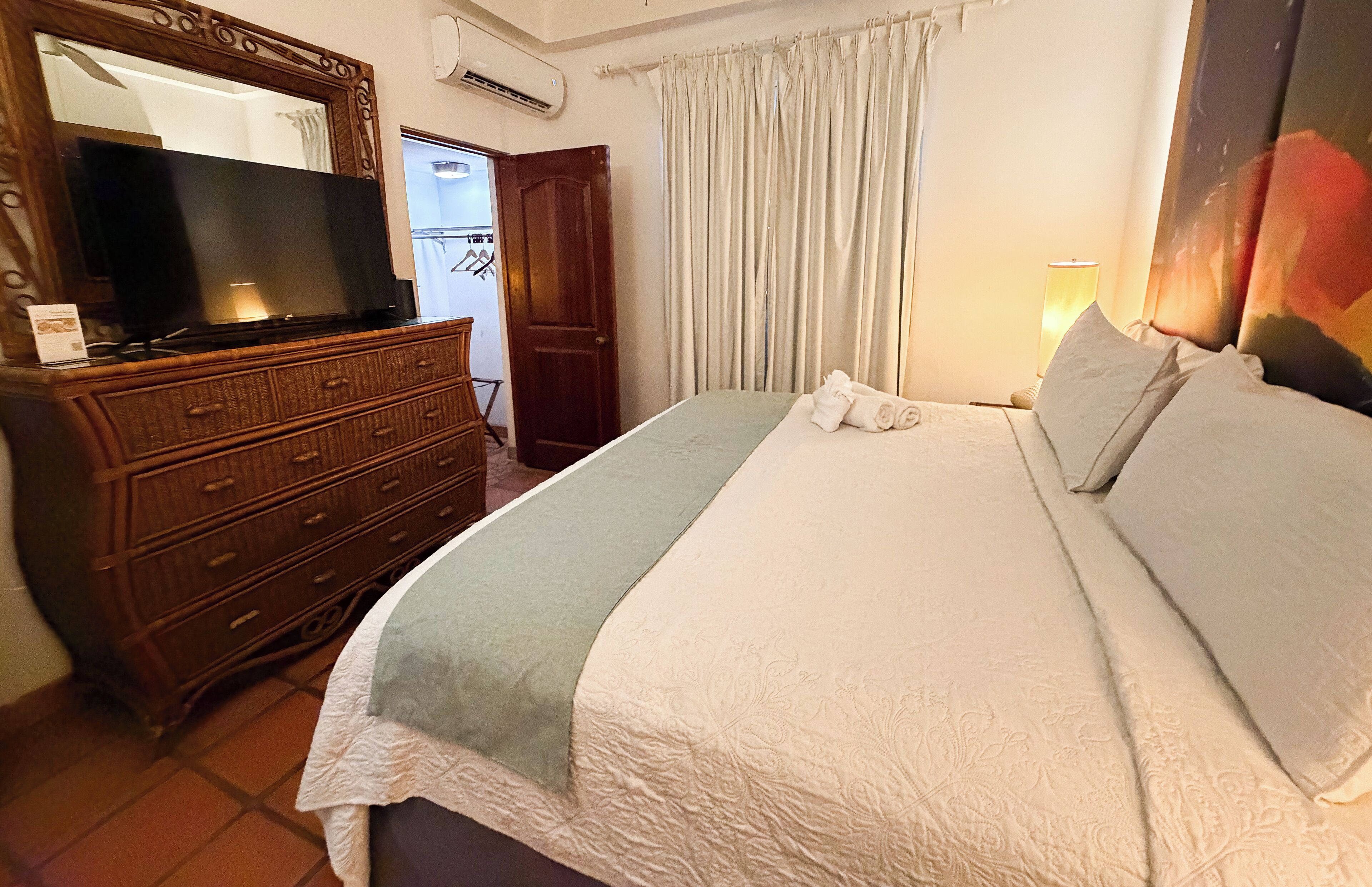 A hotel room with a large bed, a wooden dresser, a television, and a curtain.