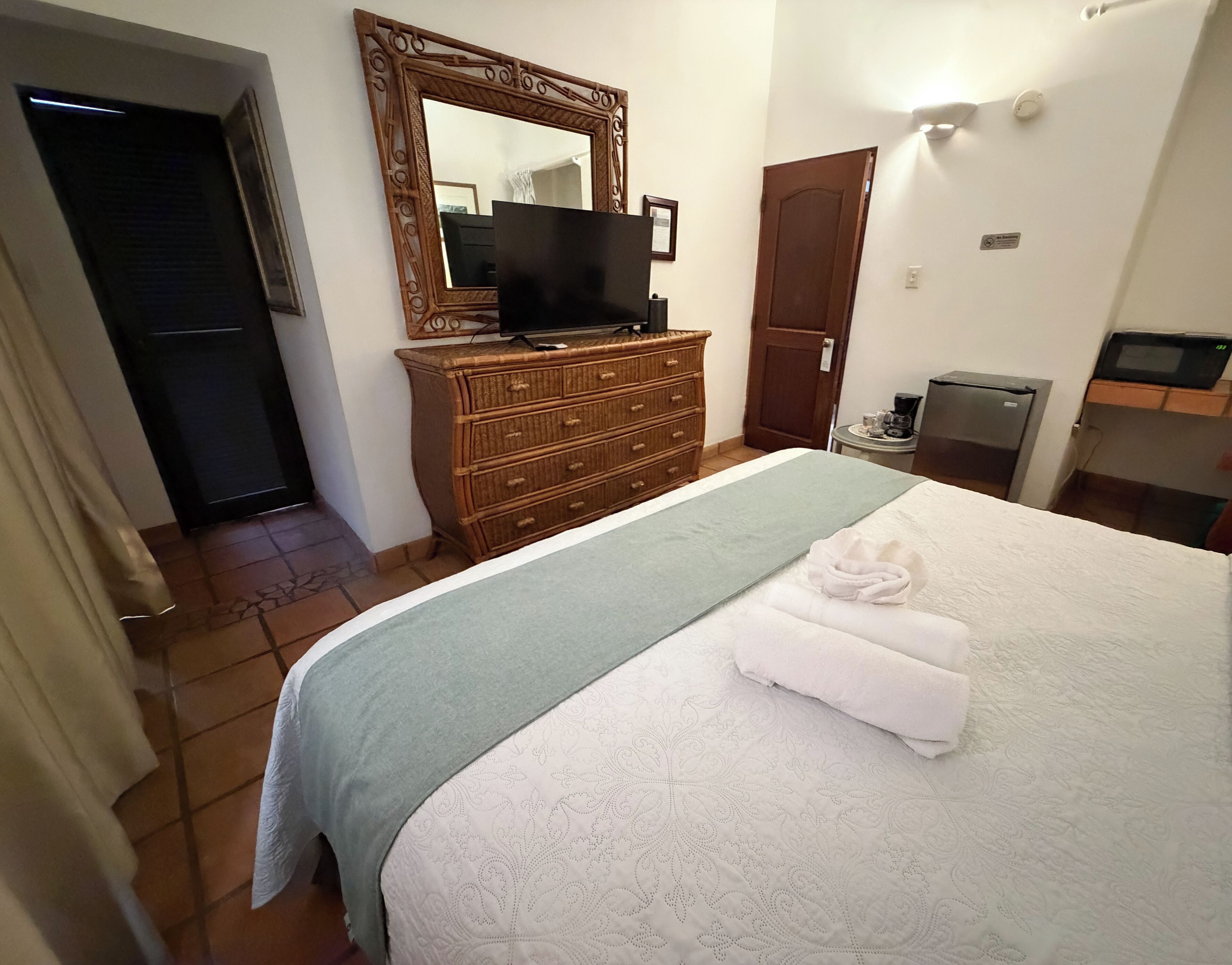 Ein Hotelzimmer mit Bett, Schminktisch, Fernseher, einer Tür und einem kleinen Tisch mit Kaffeemaschine.