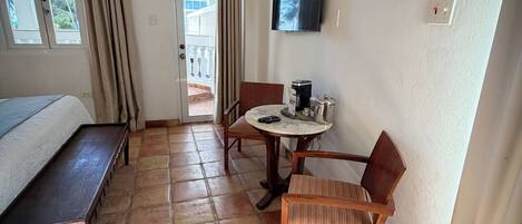 Habitación de hotel con cama, una pequeña mesa con sillas, unidad de aire acondicionado, televisor montado en la pared y vista al balcón exterior.