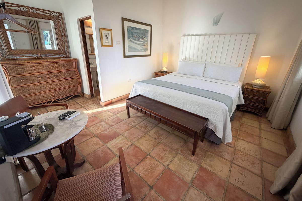 Une chambre à coucher comprenant un lit, des tables de chevet, une commode, une table ronde avec des chaises et un miroir.