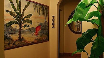A hallway with a patterned rug, a painting of a tree and bird, and a potted plant.