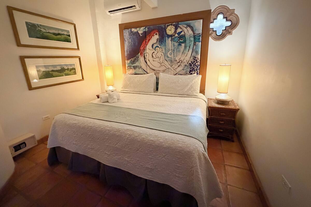Une chambre à coucher avec un lit, deux lampes de chevet, une œuvre d’art accrochée au mur et des tableaux encadrés.