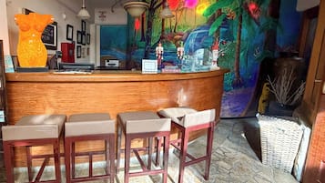 Una zona de bar con mostrador de madera, tres taburetes y un mural colorido sobre un suelo con diseño de piedra.