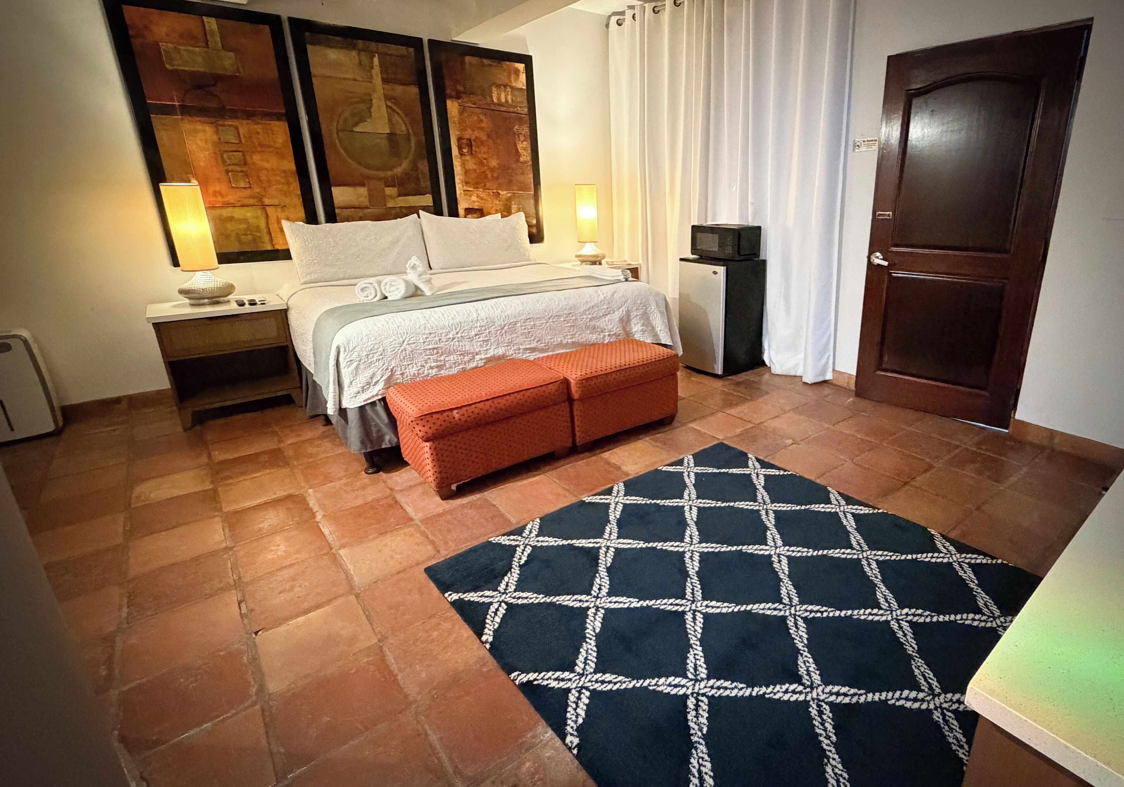Ein Schlafzimmer mit Bett, Nachttischen, einem Fernseher, einer Tür und einem gemusterten Teppich.