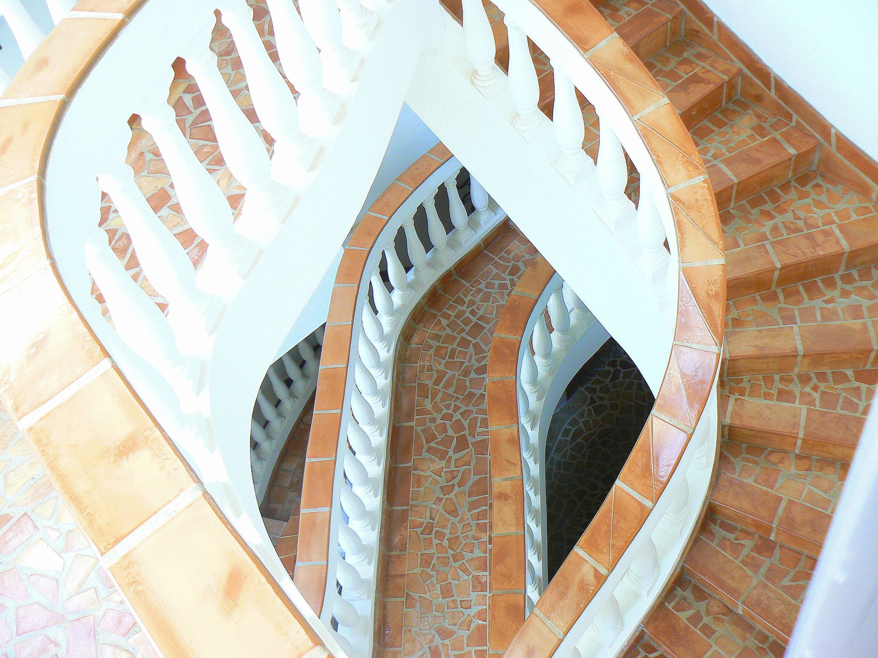Un escalier en colimaçon avec des rampes blanches et des marches recouvertes de carreaux de terre cuite.