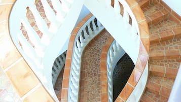 Un escalier en colimaçon avec des rampes blanches et des marches recouvertes de carreaux de terre cuite.