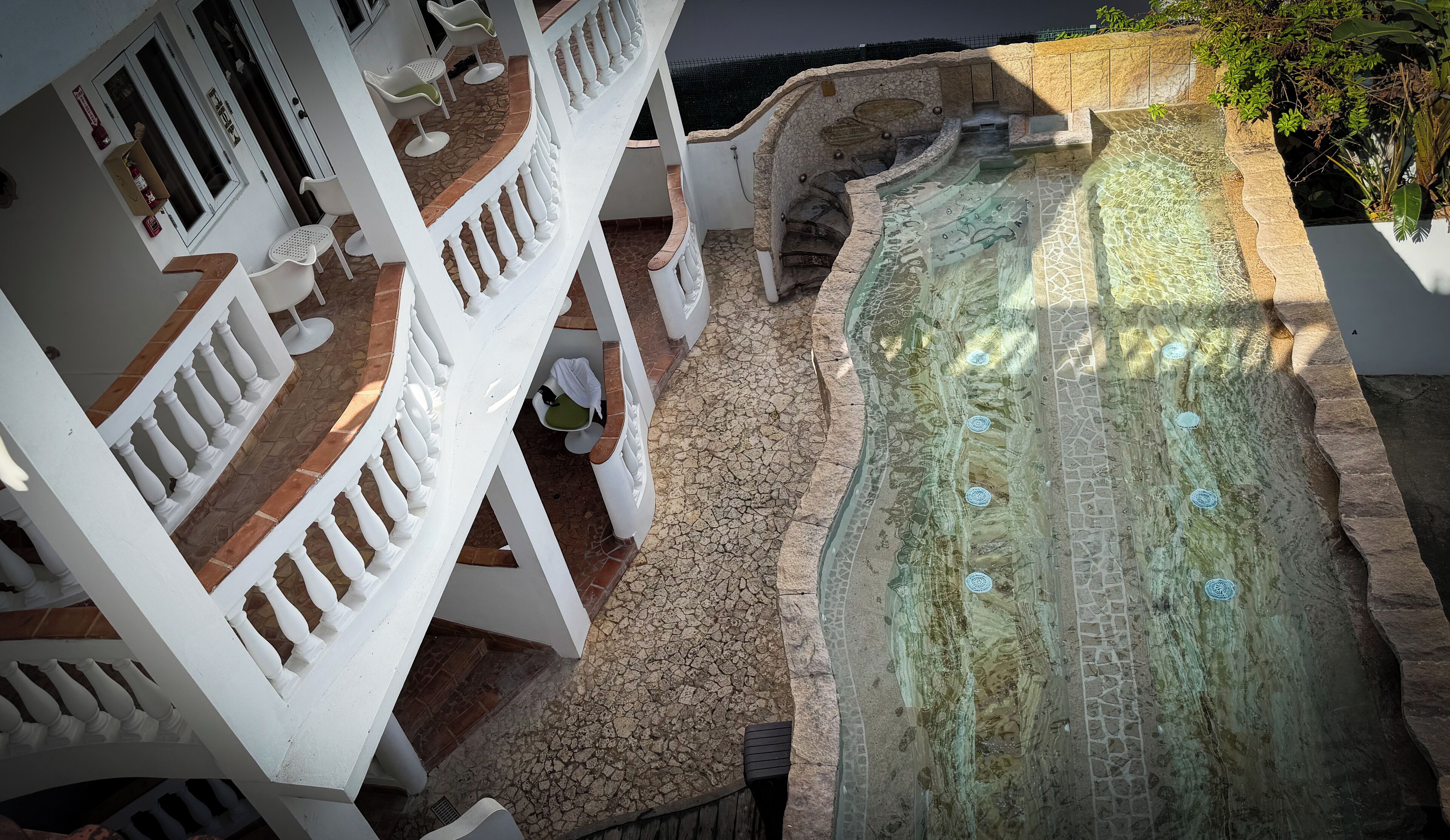 Une piscine au design en pierre, un balcon blanc avec des chaises et une vue sur la mer.